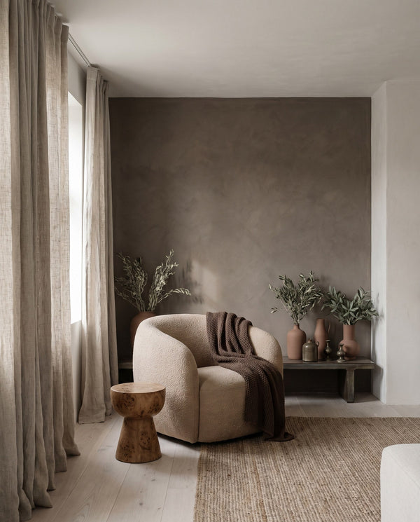 A living corner with a deep clay-coloured wall, a boucle armchair and a low timber bench