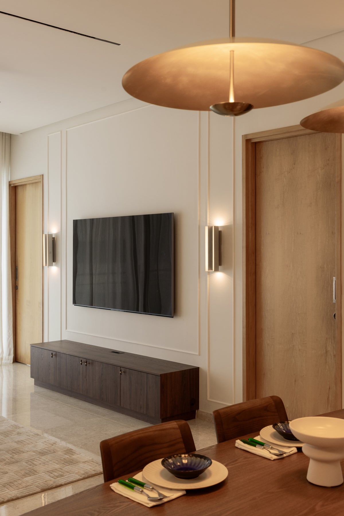 Television wall with panel mouldings, two brass wall lights and a low walnut console, in a home Sundays in Bed designed at DC Residensi, Damansara Heights, a short drive from Bukit Tunku