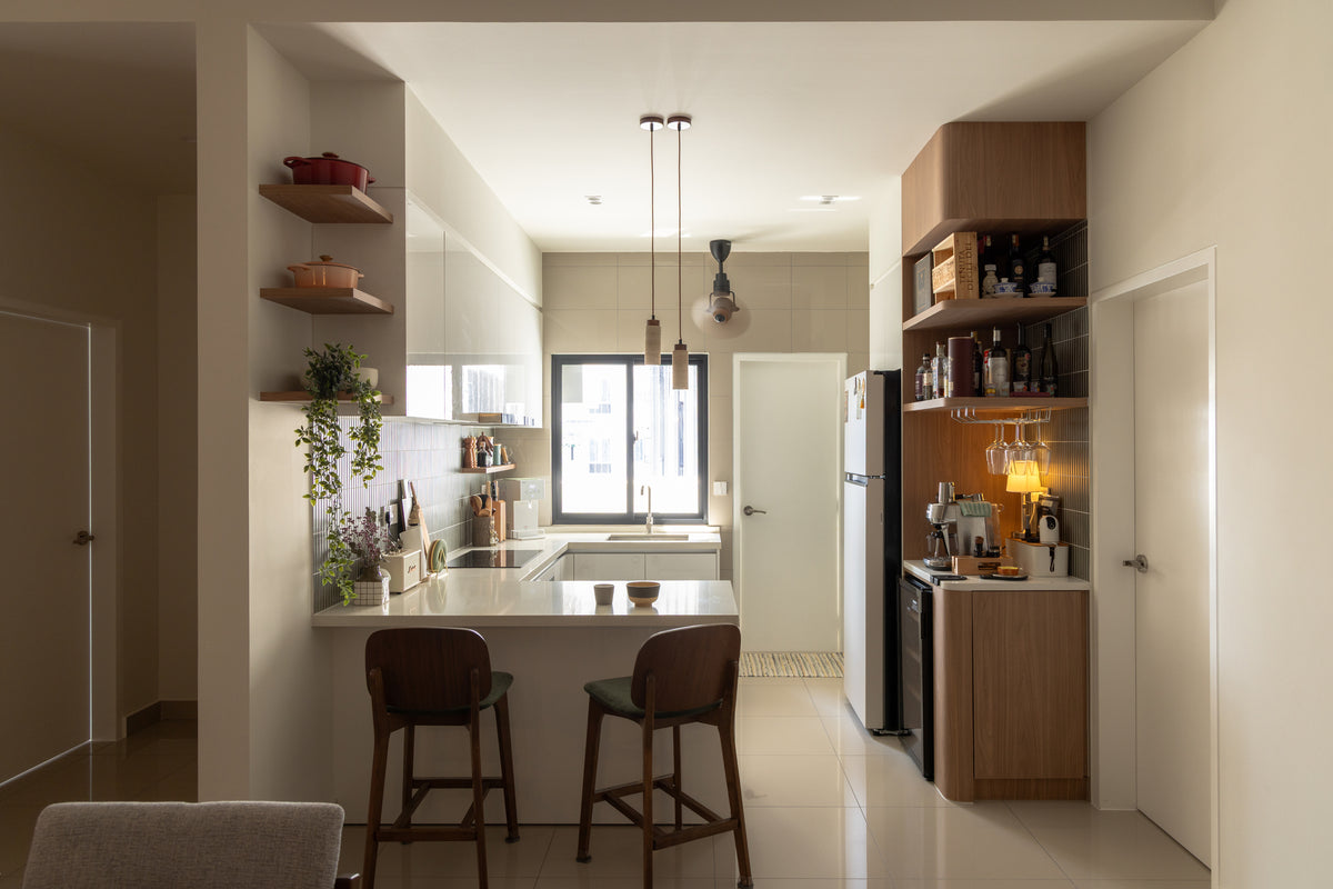 An open kitchen with a breakfast peninsula and stools, open timber shelves and a tall pantry, in a home Sundays in Bed designed at Bangsar Hill Park, Bangsar
