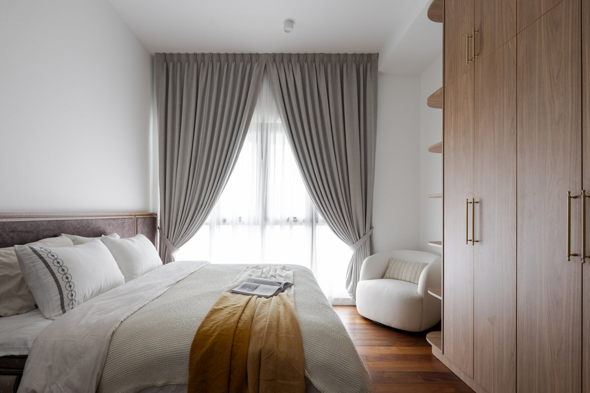 A bedroom with grey drapes over sheers, a boucle chair and a mustard throw on linen, in a home Sundays in Bed designed at Setia Sky Seputeh, Seputeh