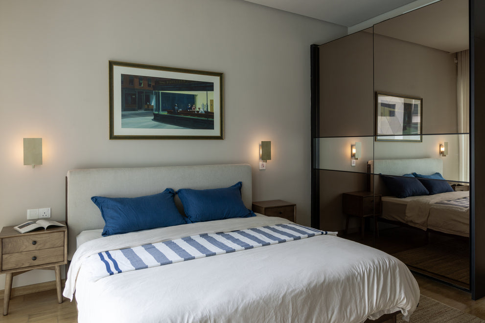 A bedroom with an upholstered bed, blue cushions, wall lights and a mirrored wardrobe, in a home Sundays in Bed designed at DC Residency, Damansara Heights