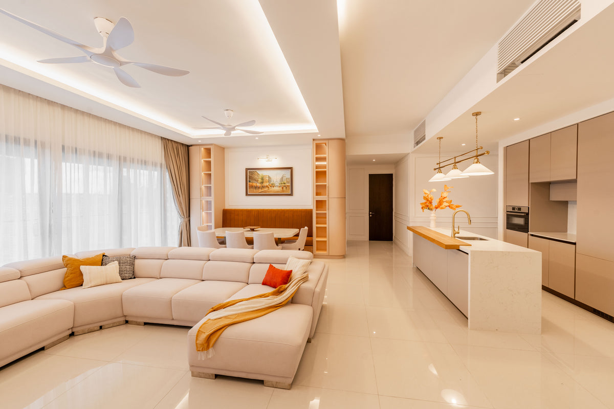 An open living room with a cream sectional, ceiling fans, sheers and the dry kitchen island beyond, in a home Sundays in Bed designed at Setia Sky Seputeh, Seputeh