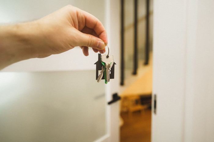 Hand holding a house key at a bright doorway into a new home