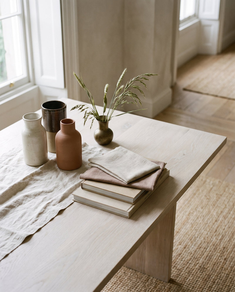 Styling still life of ceramic vessels, linen and fabric swatches on a pale oak table