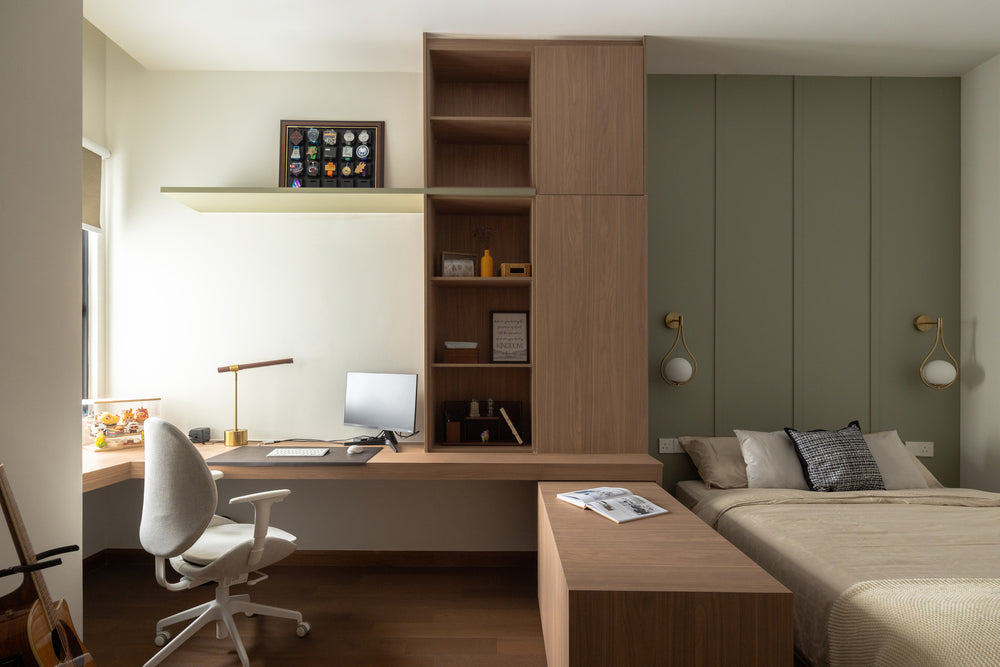 A bedroom with a built-in timber desk and shelving, a sage panelled wall behind the bed, globe wall lights and an office chair, in a home Sundays in Bed designed at Bangsar Hill Park, Bangsar