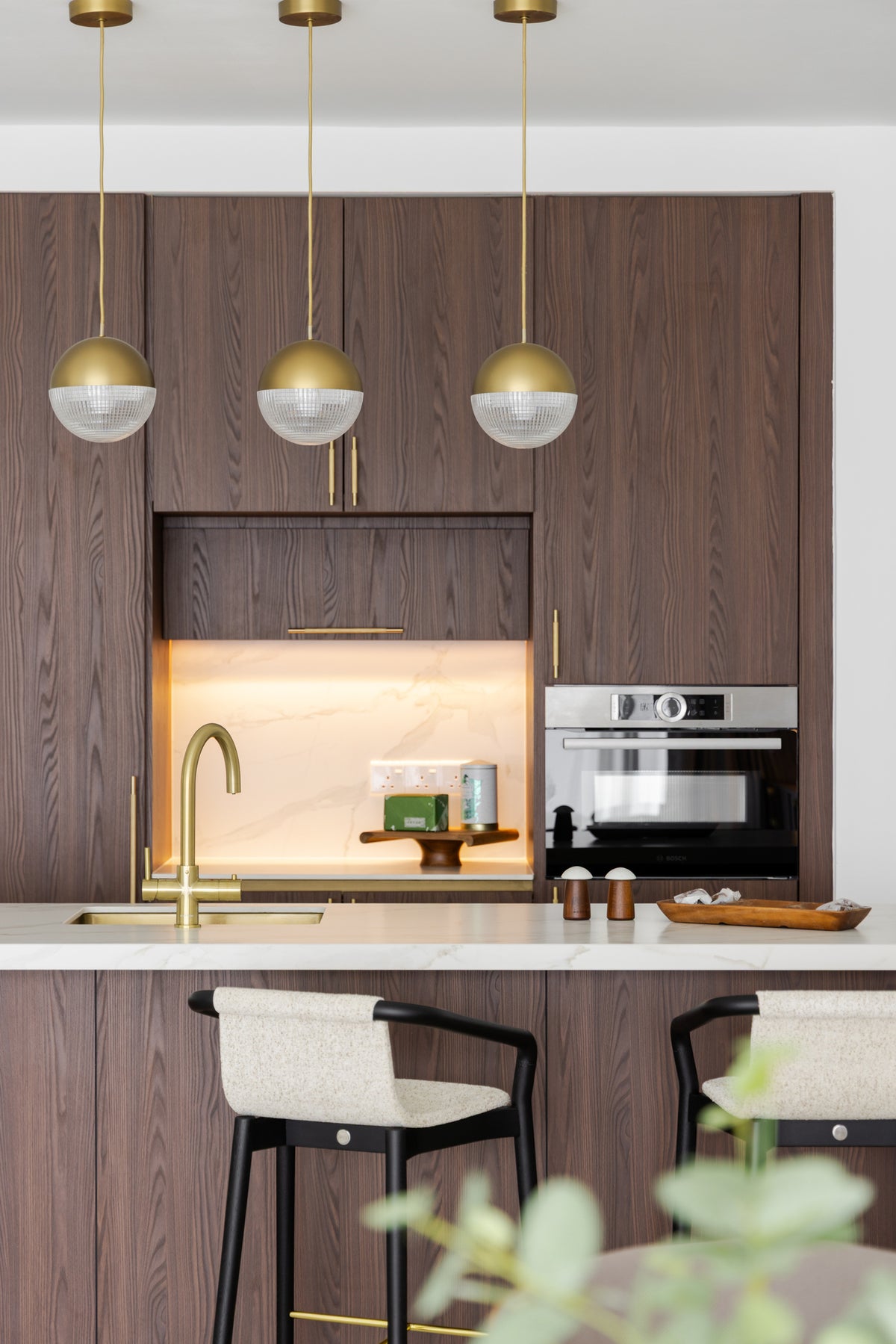 A kitchen wall with walnut, a lit marble niche and three globe pendants over stone, in a home Sundays in Bed designed at Setia Sky Seputeh, Seputeh