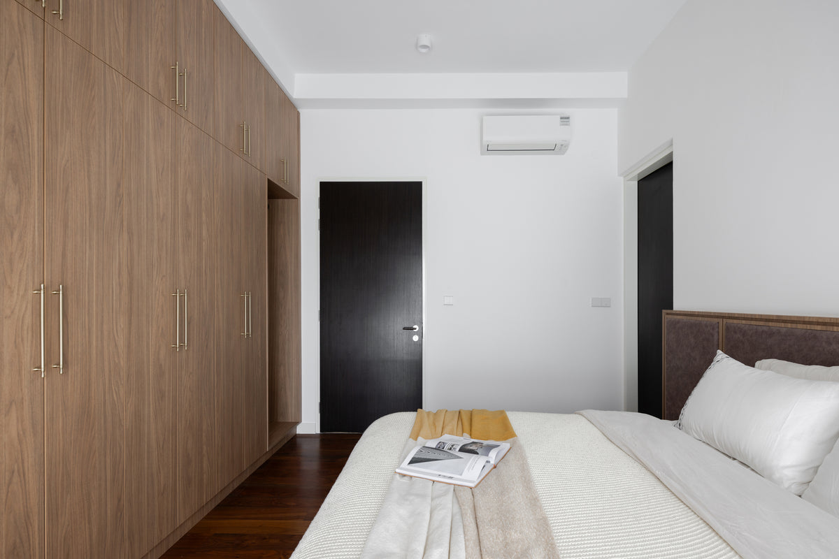 Bedroom with a full-height walnut wardrobe wall, a dark door and an upholstered bed, in a home Sundays in Bed designed at Setia Sky Seputeh