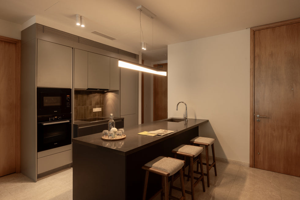 A kitchen with a dark stone island and stools, built-in ovens and tall grey cabinets, in a home Sundays in Bed designed at DC Residency, Damansara Heights