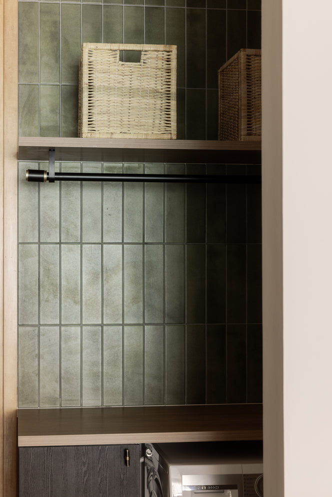 Utility corner with green handmade tiles, a hanging rail, woven baskets on a shelf and a washing machine below, in a home Sundays in Bed designed at DC Residensi, Damansara Heights