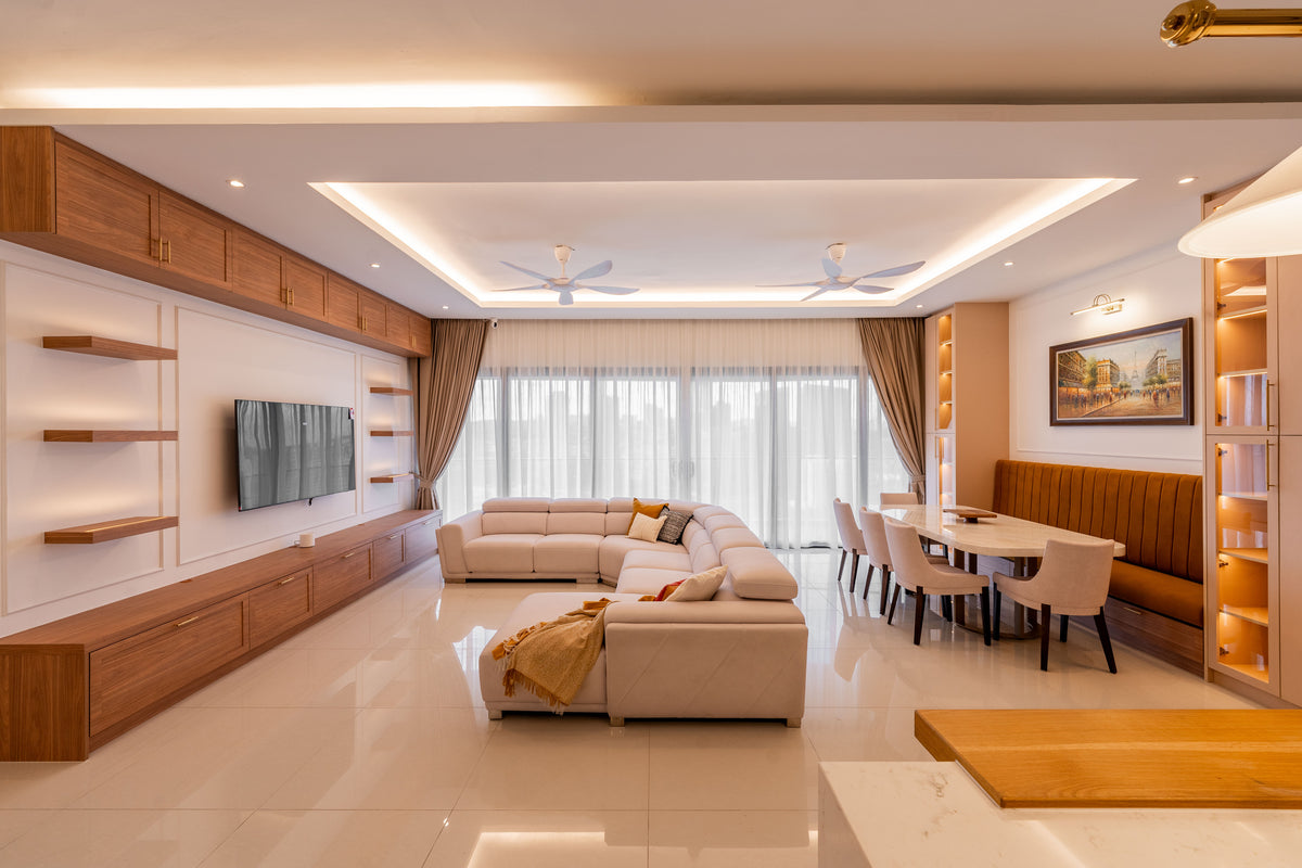 Long open-plan living and dining room with a cream sectional, a timber television wall, ceiling fans and a dining table set against an ochre banquette, in a home Sundays in Bed designed at Setia Sky Seputeh