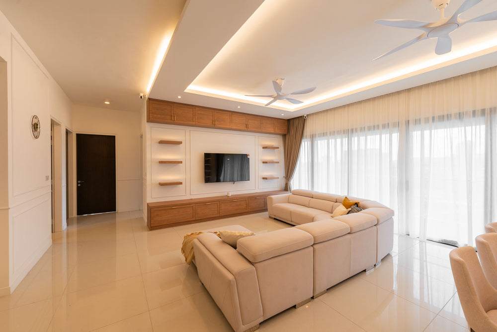 Living room with a timber television wall and open shelves, a cream sectional sofa, ceiling fans and full-height sheer curtains along the windows, in a home Sundays in Bed designed at Setia Sky Seputeh