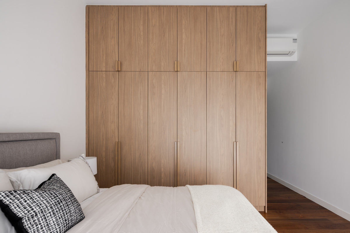 A bedroom we designed at Setia Sky Seputeh: a wood-grain wardrobe wall to the ceiling behind a bed with a grey headboard and a tweed cushion.
