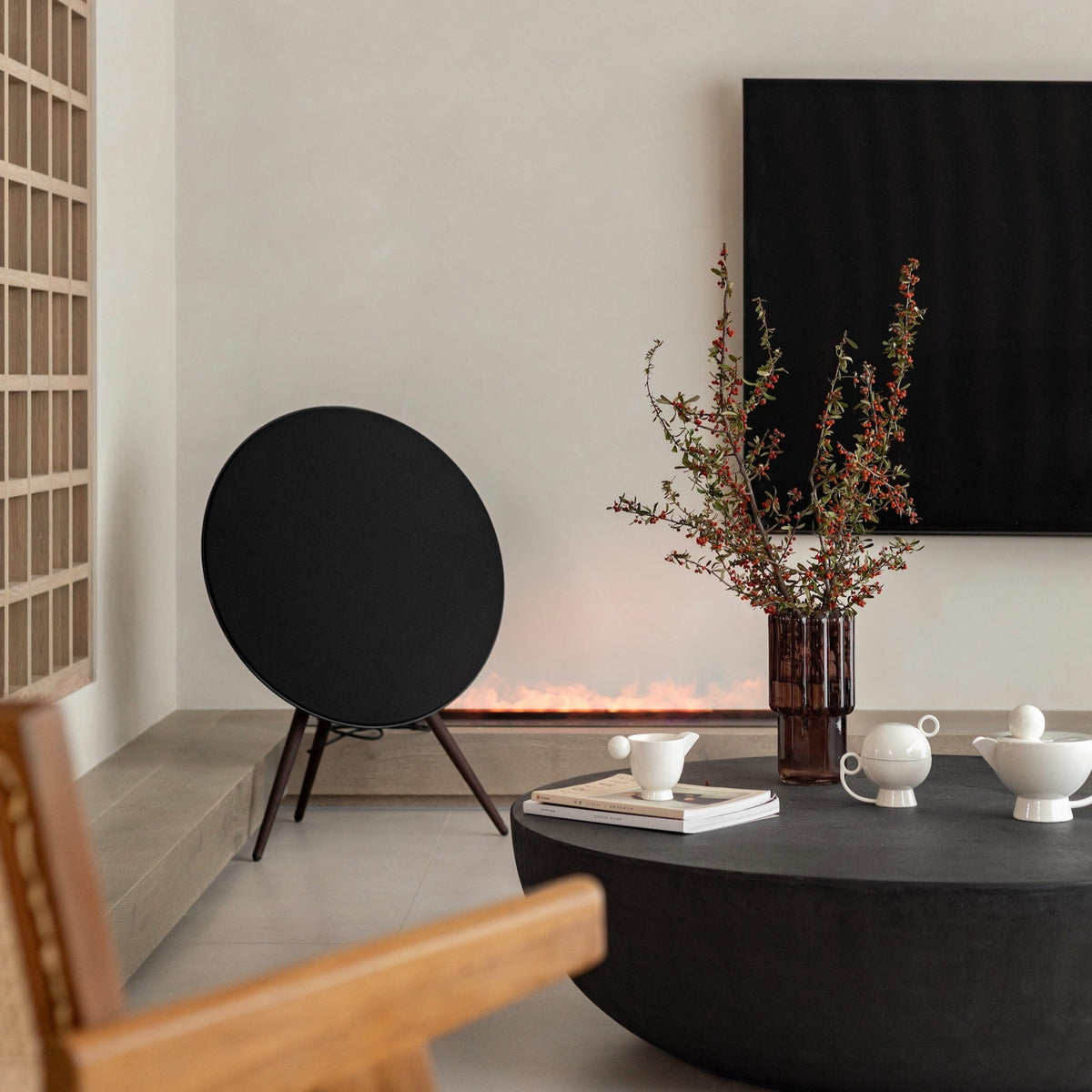 A living room with a low round table, ceramics, a speaker and red berry stems in a glass vase